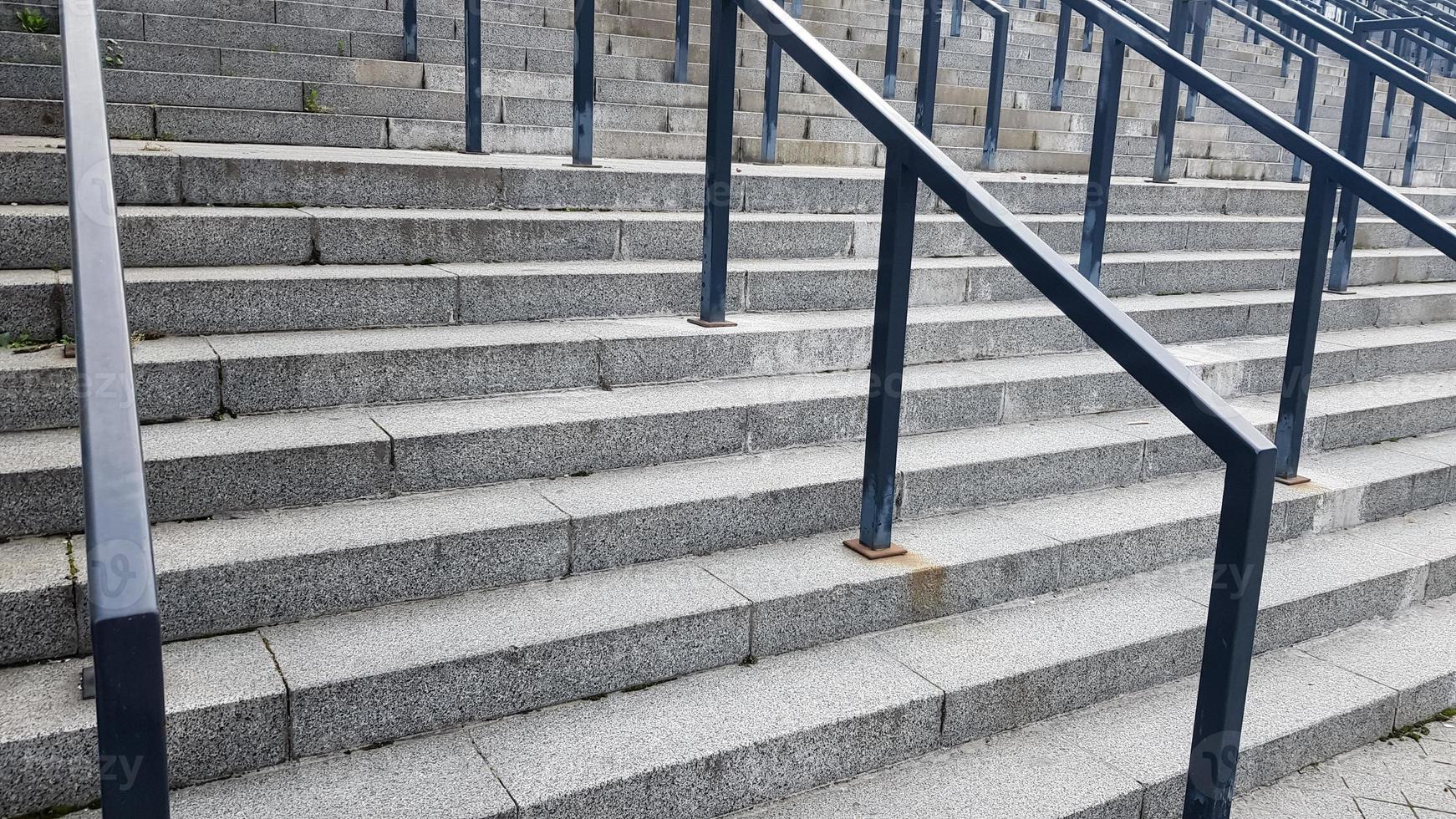 External multi-stage stone staircase. There are a lot of stairs and railings made of metal. Many steps in an urban environment, symbolic abstract background. photo
