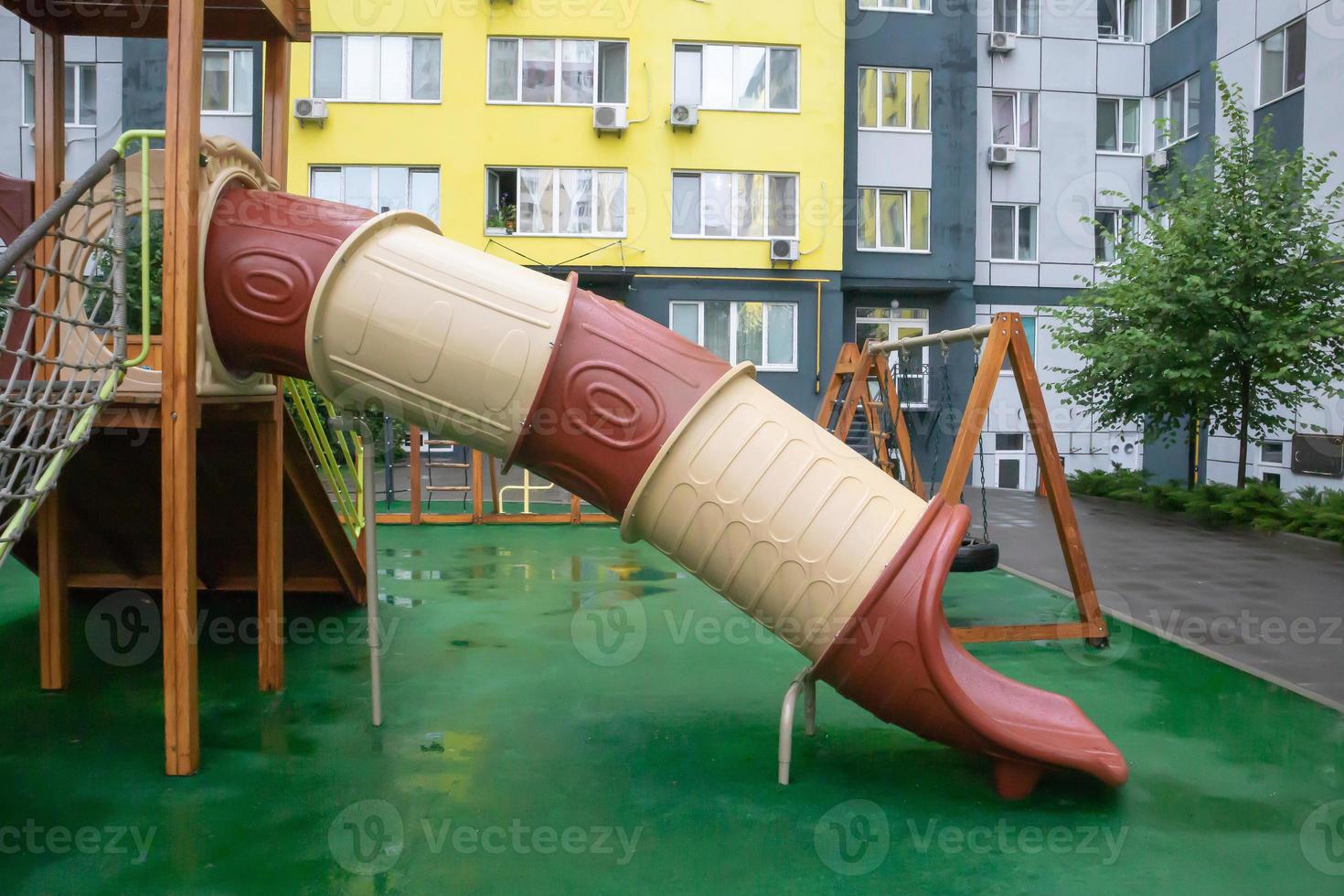A courtyard of high-rise buildings with a modern and large playground made of wood and plastic on a rainy summer day without people. Empty outdoor playground. A place for children's games and sports. photo