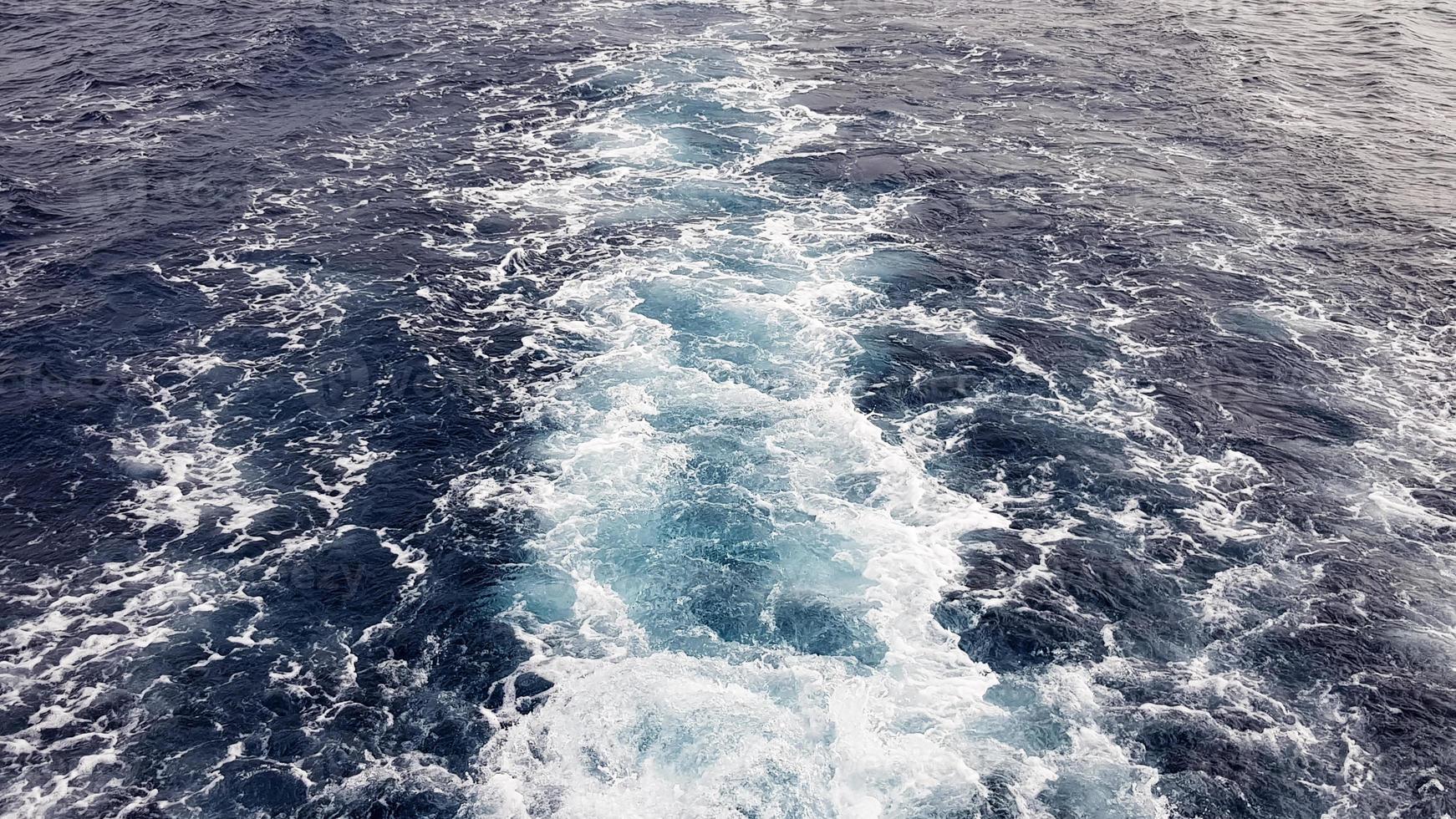 Cruise ship or trail on the surface of the blue red sea. Sea water ship trail with white foamy wave. Top view of the deep ocean. Perspective of a wave of white water. photo