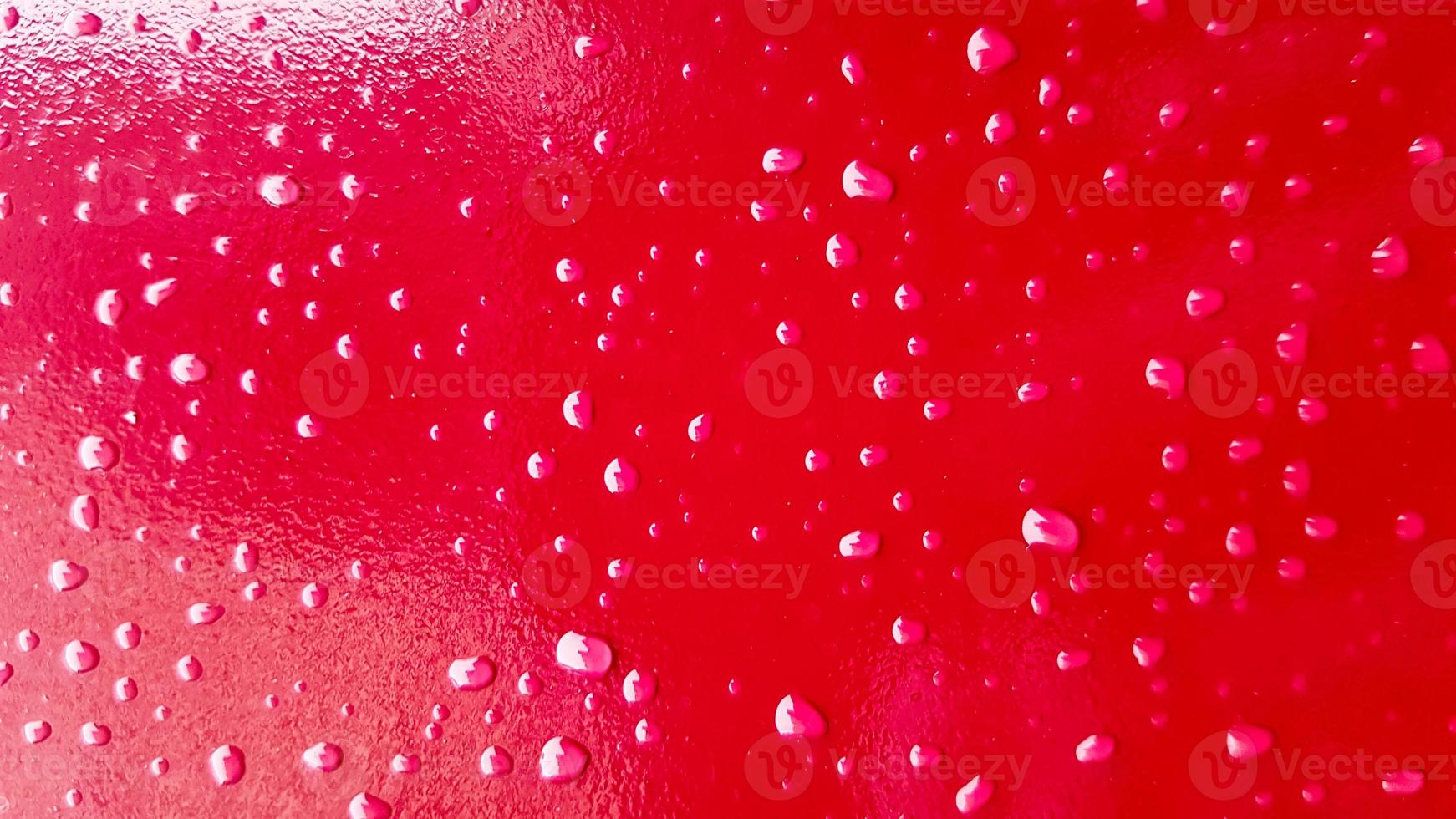 coche rojo después de la lluvia. las gotas de agua se acumulan en la parte superior de la superficie metálica. Gotas de agua roja sobre fondo abstracto foto