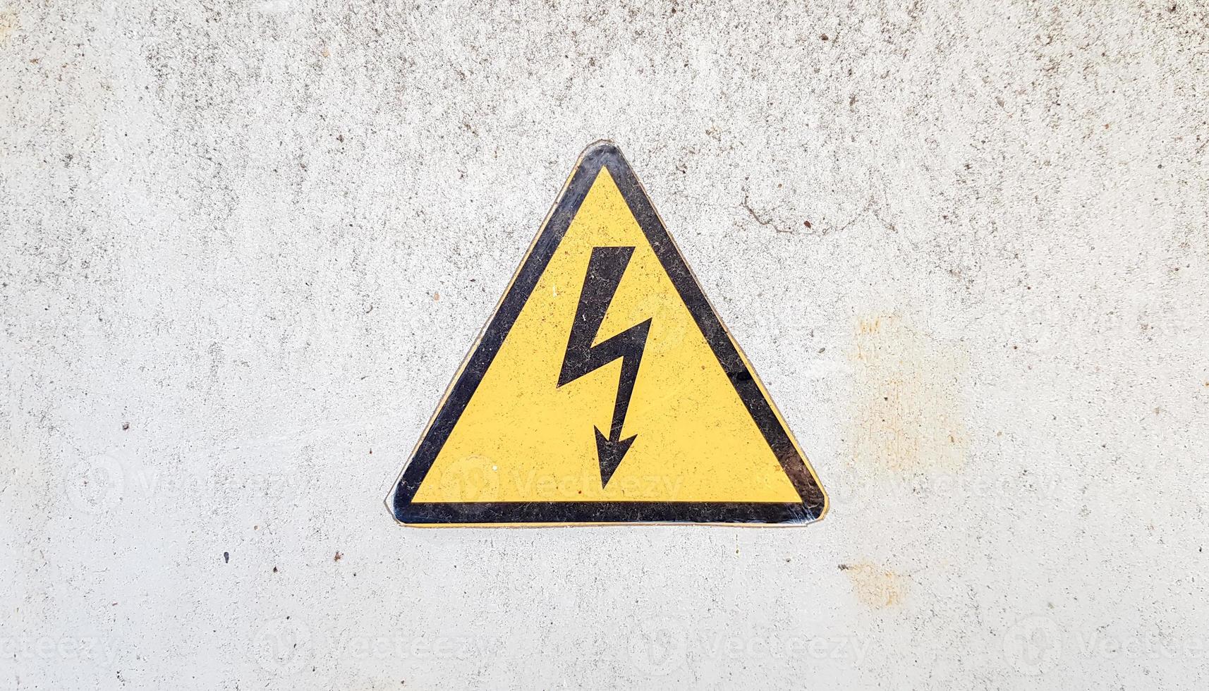 Señal de peligro de electricidad de alto voltaje. cartel triangular amarillo con un rayo en el centro. esta advertencia está escrita en una superficie de metal vieja pintada con pintura gris. foto