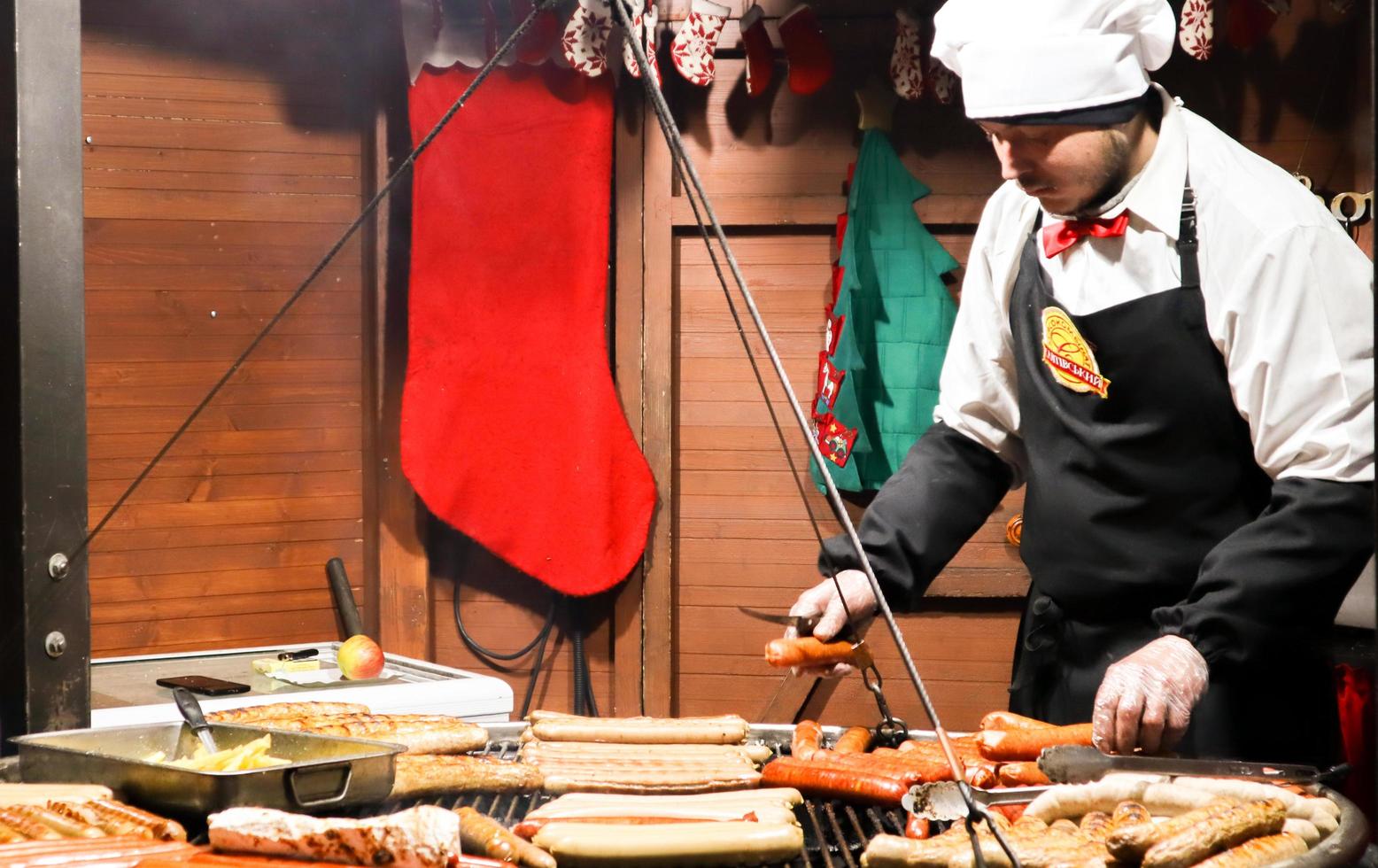 Ucrania, Kiev - 3 de enero de 2019. Un chef cocina una barbacoa a la parrilla, comida callejera, festival de comida. salchicha fresca y perritos calientes a la parrilla al aire libre. un hombre está preparando comida callejera de la cocina alemana foto