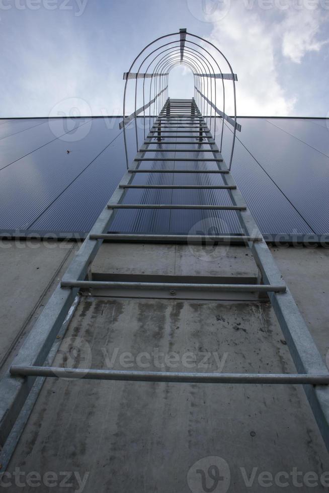 Fire escape on the industrial building above, bottom view. Stainless steel handrails, roof ladder. Detail view of stairs with safety cage. Building construction concept. photo