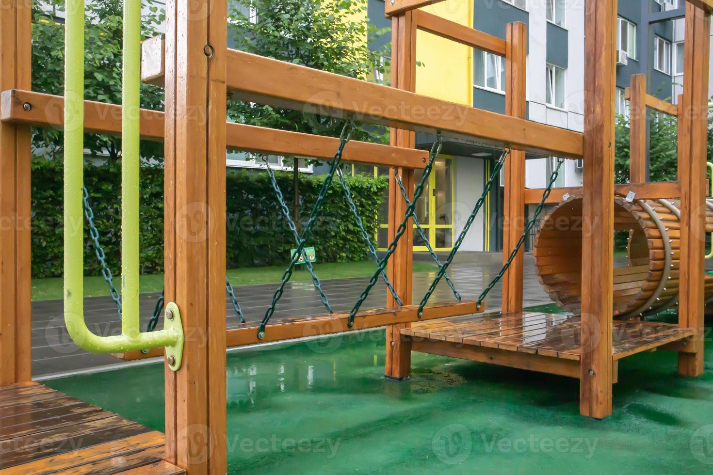 A courtyard of high-rise buildings with a modern and large playground made of wood and plastic on a rainy summer day without people. Empty outdoor playground. A place for children's games and sports. photo