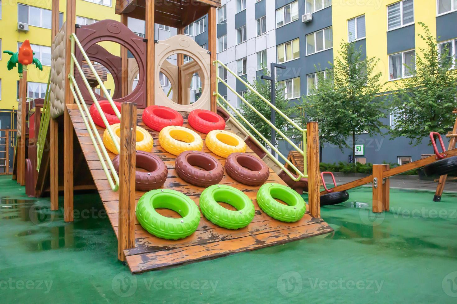 A courtyard of high-rise buildings with a modern and large playground made of wood and plastic on a rainy summer day without people. Empty outdoor playground. A place for children's games and sports. photo