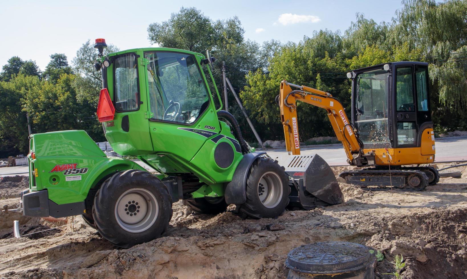 Two small excavators on a large construction site. Bright green on wheels and yellow on tracks. Earthworks and construction. Shovel excavator. Mini loaders. Ukraine, Kiev - August 28, 2021. photo