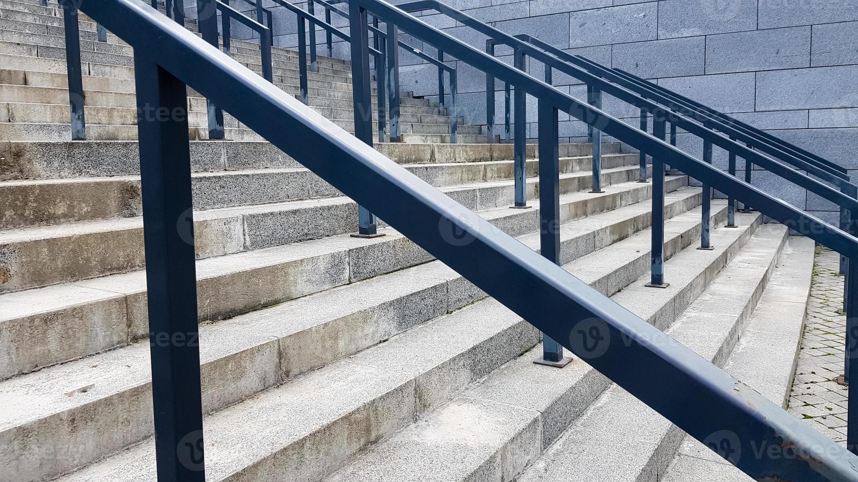External multi-stage stone staircase. There are a lot of stairs and railings made of metal. Many steps in an urban environment, symbolic abstract background. photo