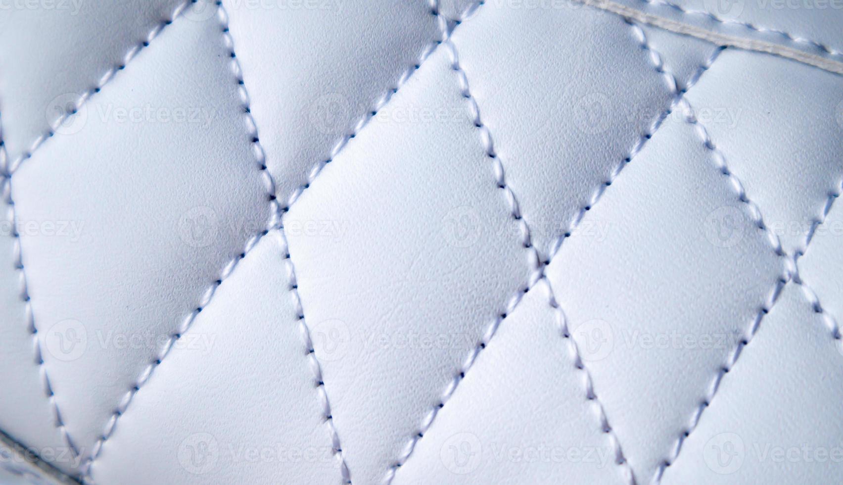 Close-up of synthetic fabric with white diamond stitching. Texture the diamond in a classic style. Luxurious background. Quilted fabric in white or light color, texture. photo