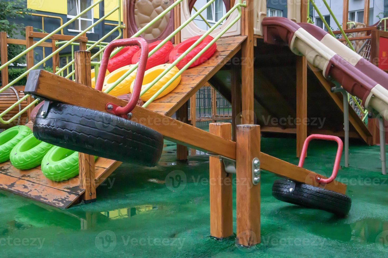 A courtyard of high-rise buildings with a modern and large playground made of wood and plastic on a rainy summer day without people. Empty outdoor playground. A place for children's games and sports. photo