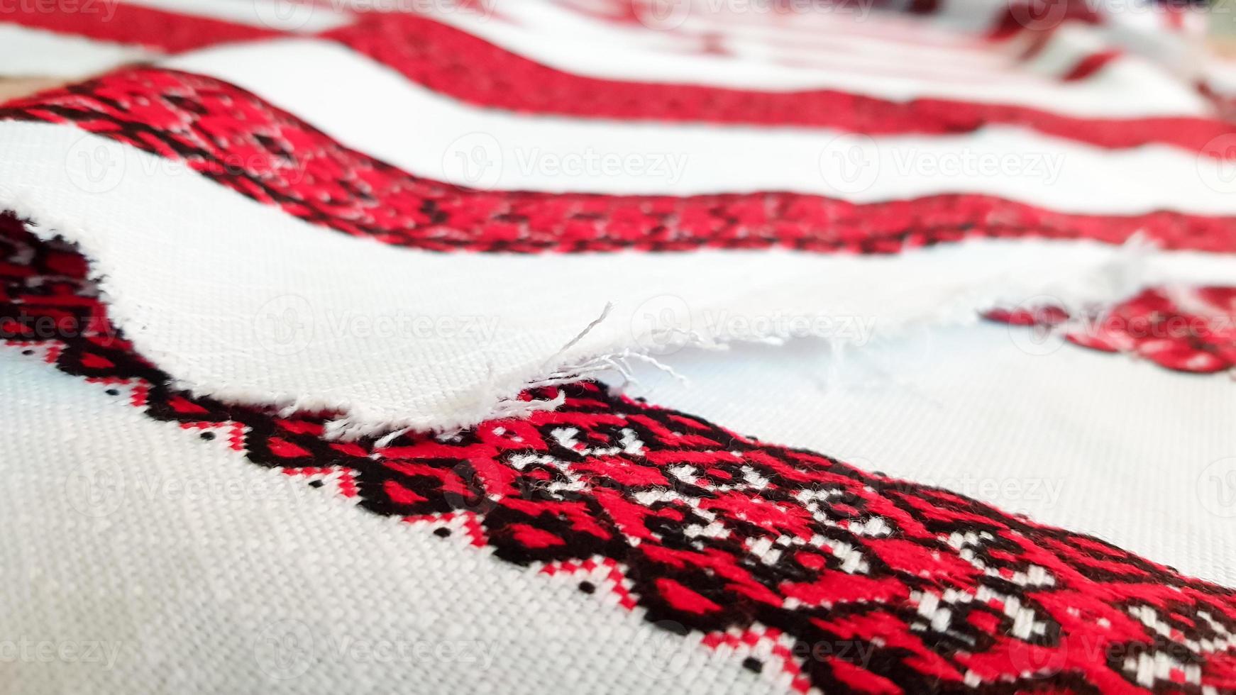Ukrainian folk hand embroidery. Embroidered ornament with red-black threads on white fabric. Embroidered ornament in black and red thread. Ethnic Ukrainian folk embroidery on white fabric. photo
