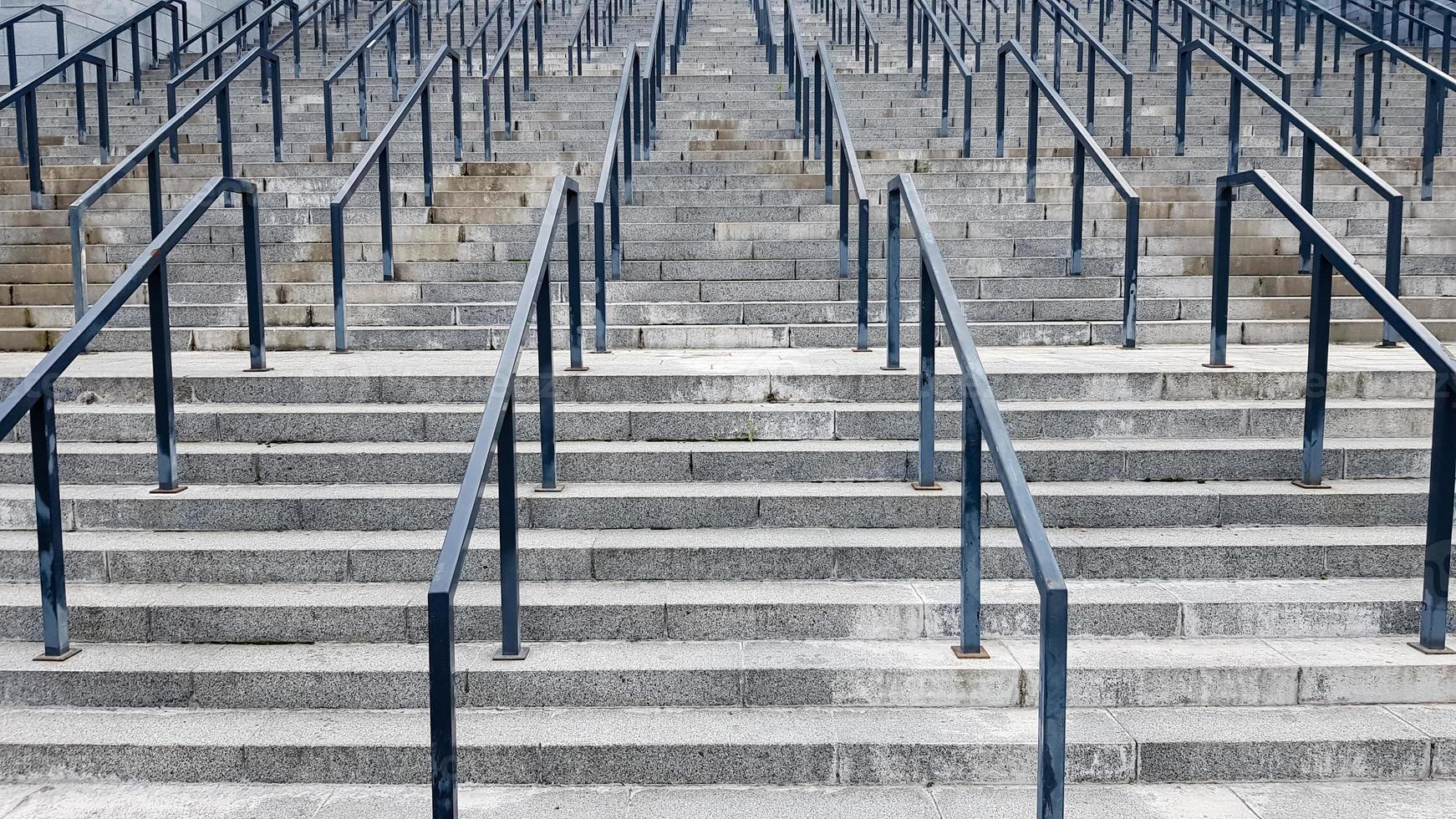 External multi-stage stone staircase. There are a lot of stairs and railings made of metal. Many steps in an urban environment, symbolic abstract background. photo