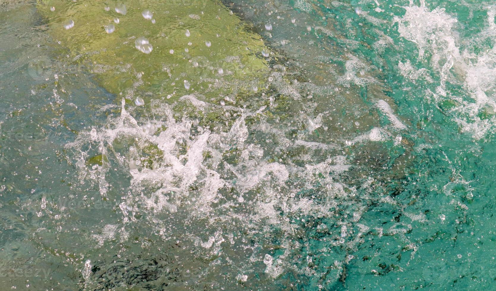 frecuentes gotas de agua en una fuente en cámara lenta caen sobre una superficie de agua limpia con salpicaduras y burbujas. chorros de agua brillan bajo el sol. el spray se extiende lentamente hacia los lados. de cerca. foto