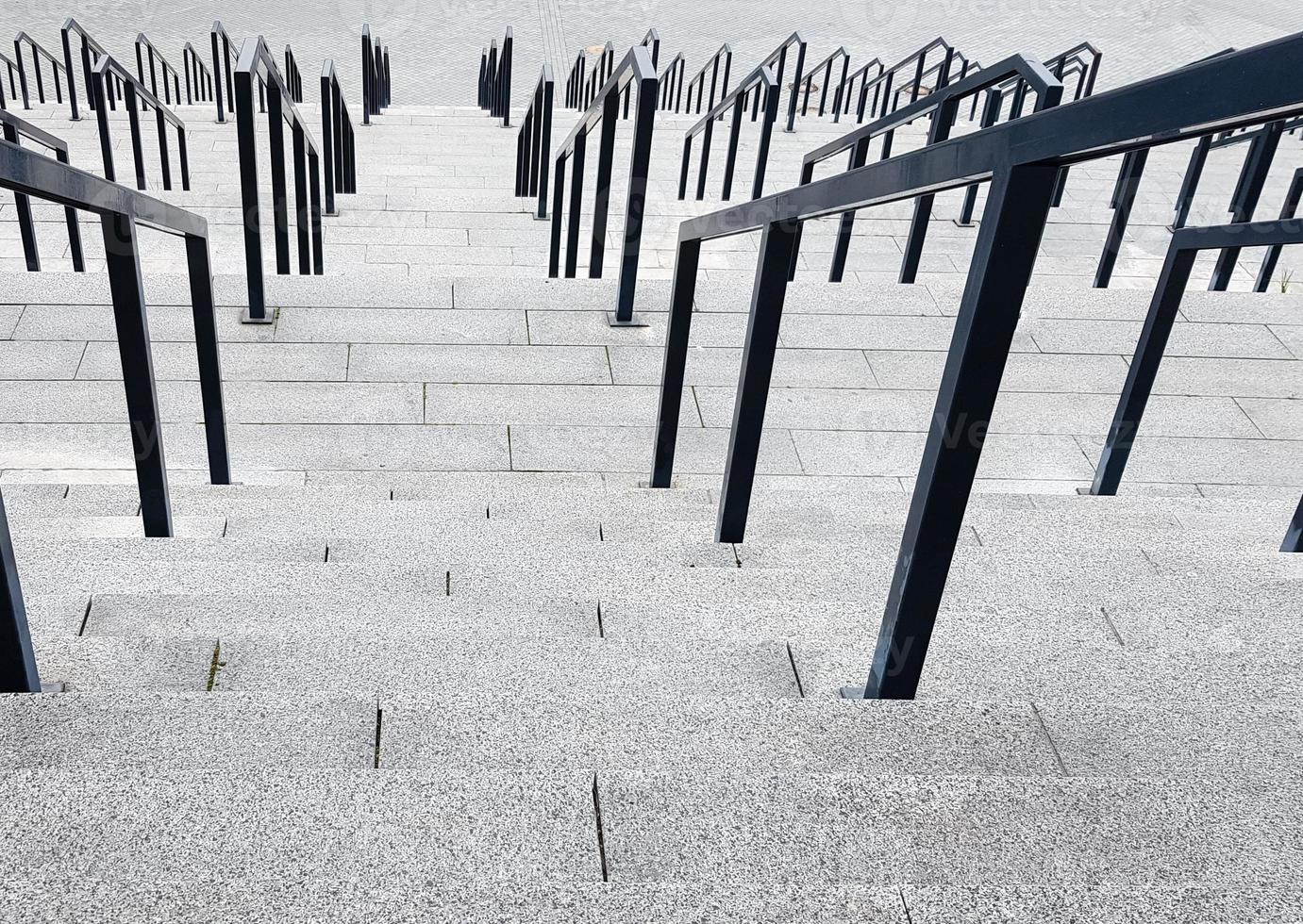 External multi-stage stone staircase. There are a lot of stairs and railings made of metal. Many steps in an urban environment, symbolic abstract background. photo