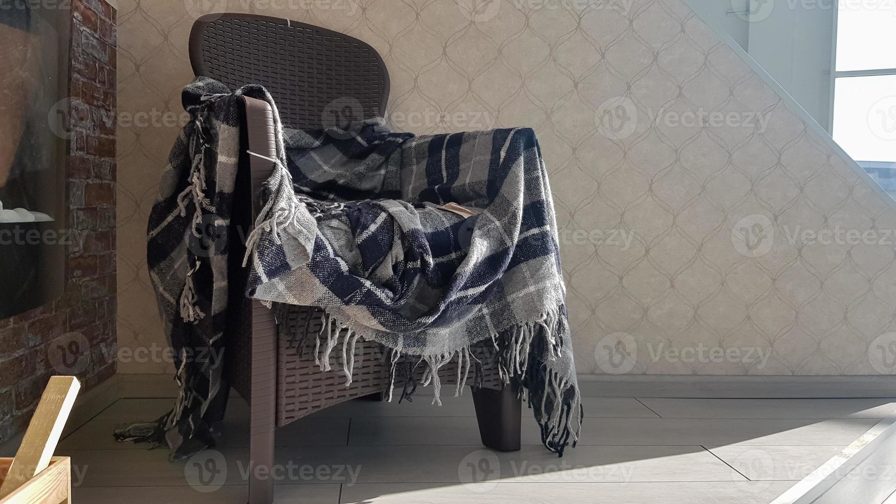 una moderna silla de plástico de mimbre con un plaid a cuadros en una casa o apartamento. el concepto de comodidad y tranquilidad en el hogar. primer plano de una silla con una tela escocesa de mimbre en la terraza con el lado. foto