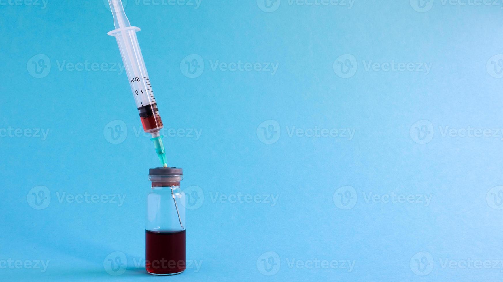 Vacunas contra la gripe y la pandemia de coronavirus, jeringa y vial con líquido rojo sobre un fondo azul. concepto médico, inyección subcutánea, tratamiento de la enfermedad. Copie el espacio para texto o logotipo. foto