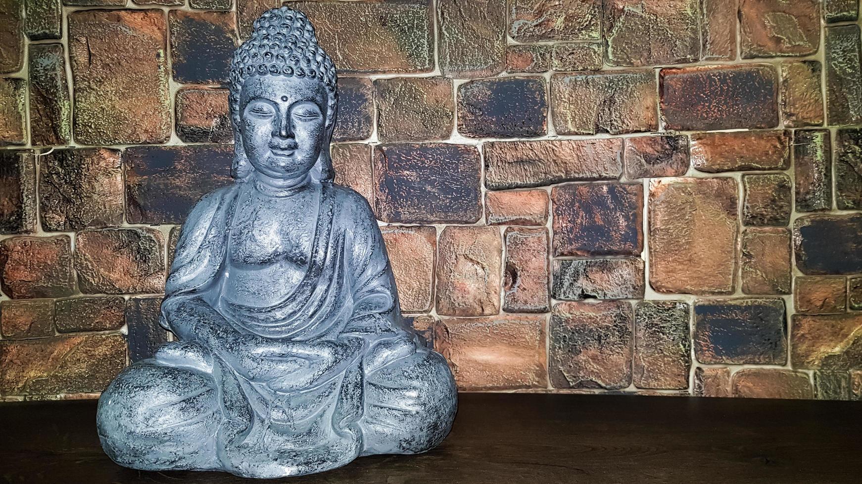 Ukraine, Kiev - June 10, 2020. Statuette of the blessing of Buddha on a wooden shelf against a stone wall. Ceramic figurines and figurines decoration or symbol in the home interior. photo