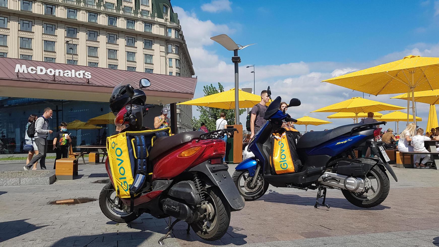 Ukraine, Kiev - August 29, 2020. Lot of parked mopeds with yellow bags with Glovo logo near McDonald's. Courier service that delivers goods ordered through a mobile application. Editorial photography. photo