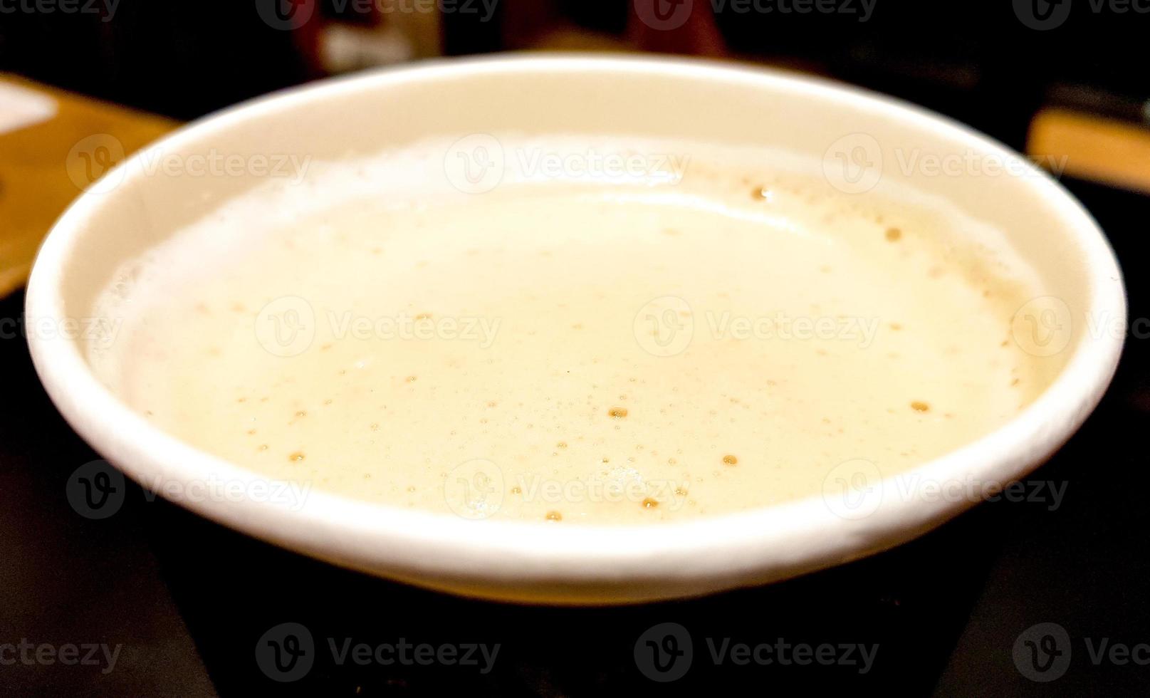 Vista superior de cerca de una taza de café de papel con leche y espuma sobre un fondo oscuro del interior del café foto