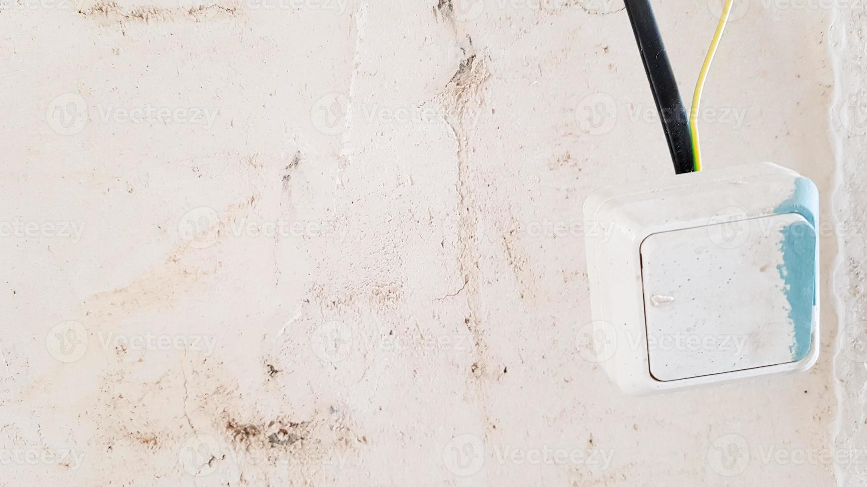 one white light switch in paint and putty is temporarily hanging on a black wire during repair against the background of an unfinished wall. open the wires. photo