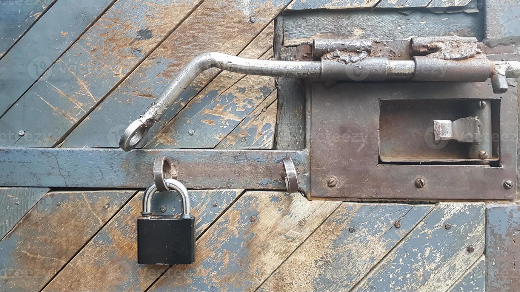 A wood weathered, texture plank door with a padlock, latch and metal fittings. photo