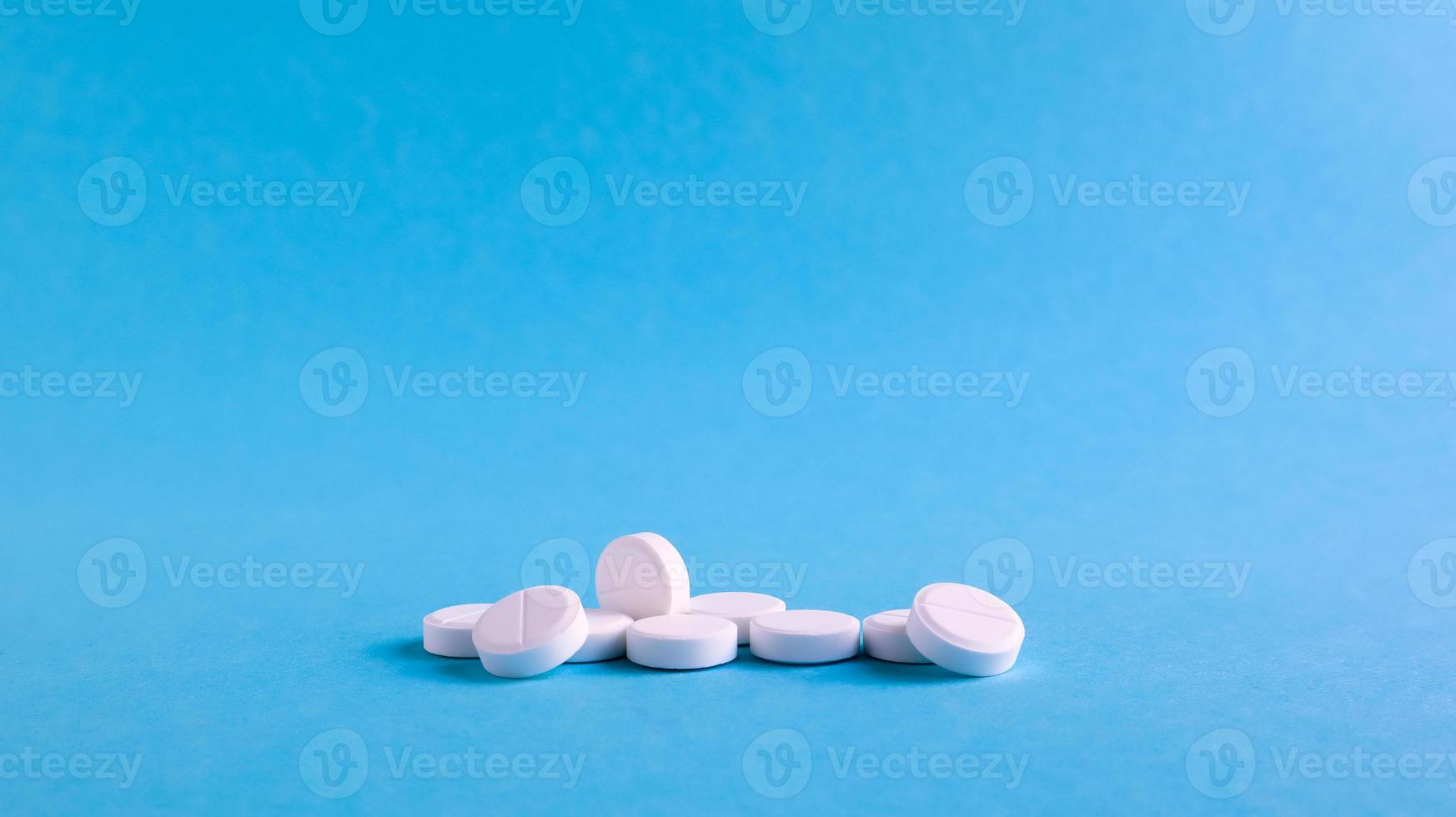 White round medical pills on a blue background. Scattered white pills on the table. The concept of medicine, pharmacy and healthcare. Copy space Empty space for text or logo. photo