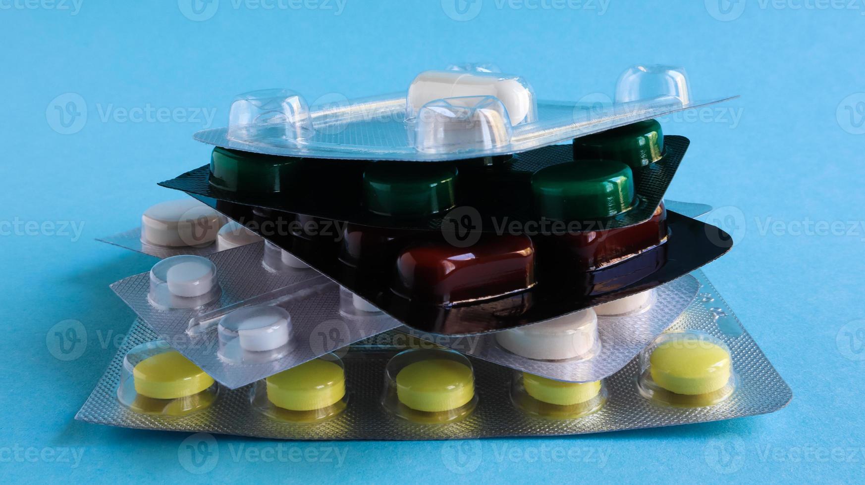 Packs of pills of various shapes and colors are stacked on a blue background. Capsules are packaged in blister packs. Different medicines. Drug treatment. Health photo. Copy space. photo