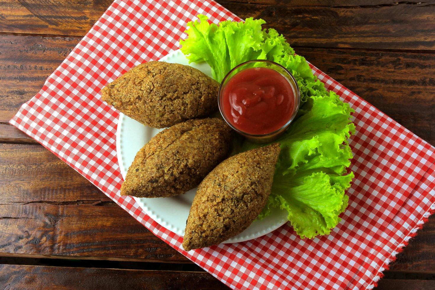 Kibbeh frito con salsa de tomate en un plato, sobre una mesa de madera rústica foto