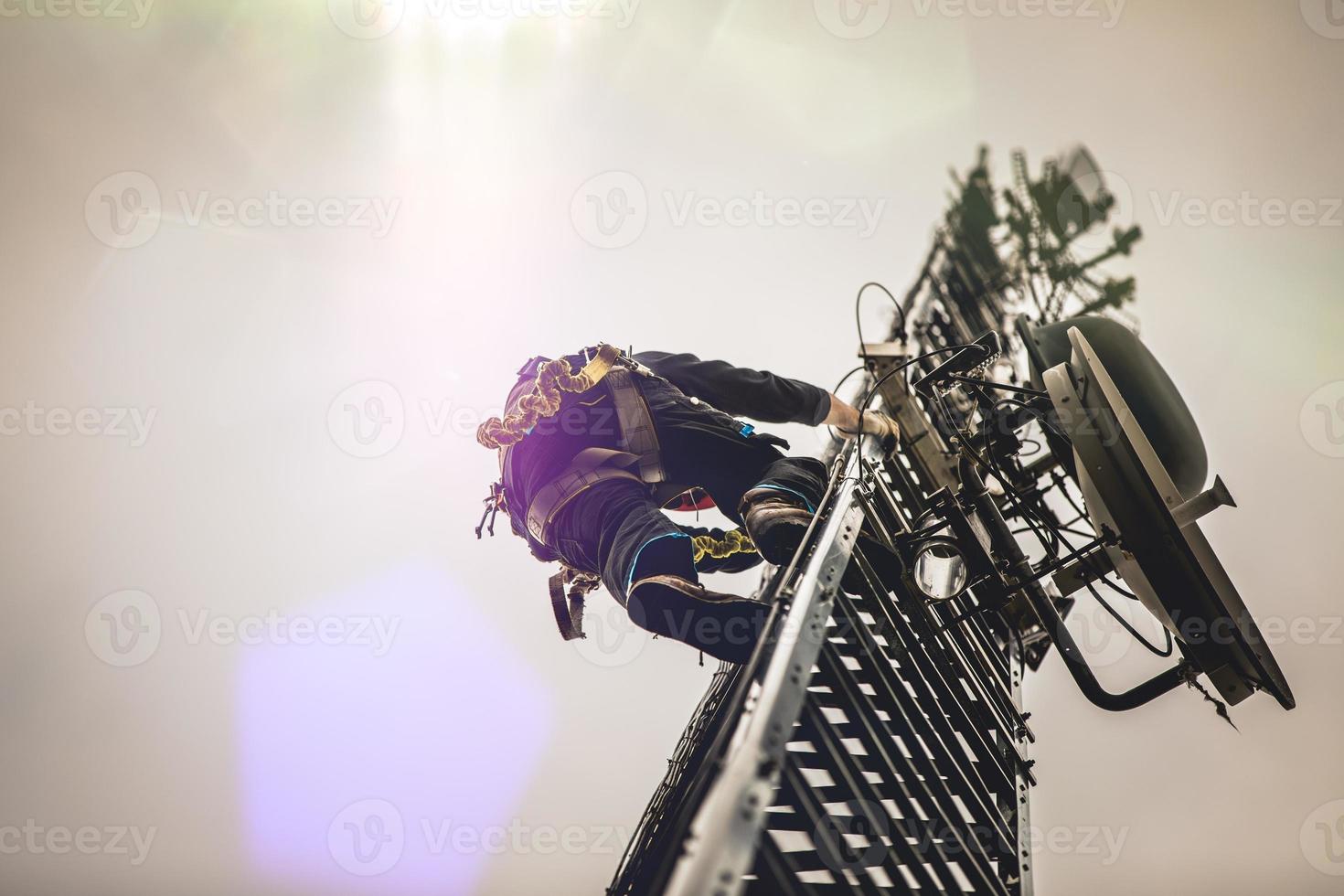Telecom Worker Climbing Antenna Tower with Harness and Tools photo