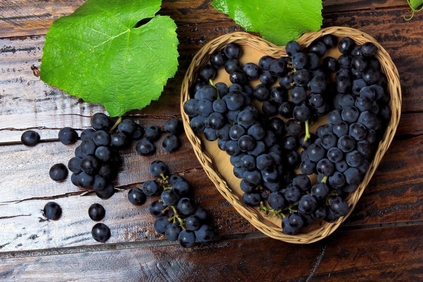 bunches of grape inside basket with heart shape on wooden table photo