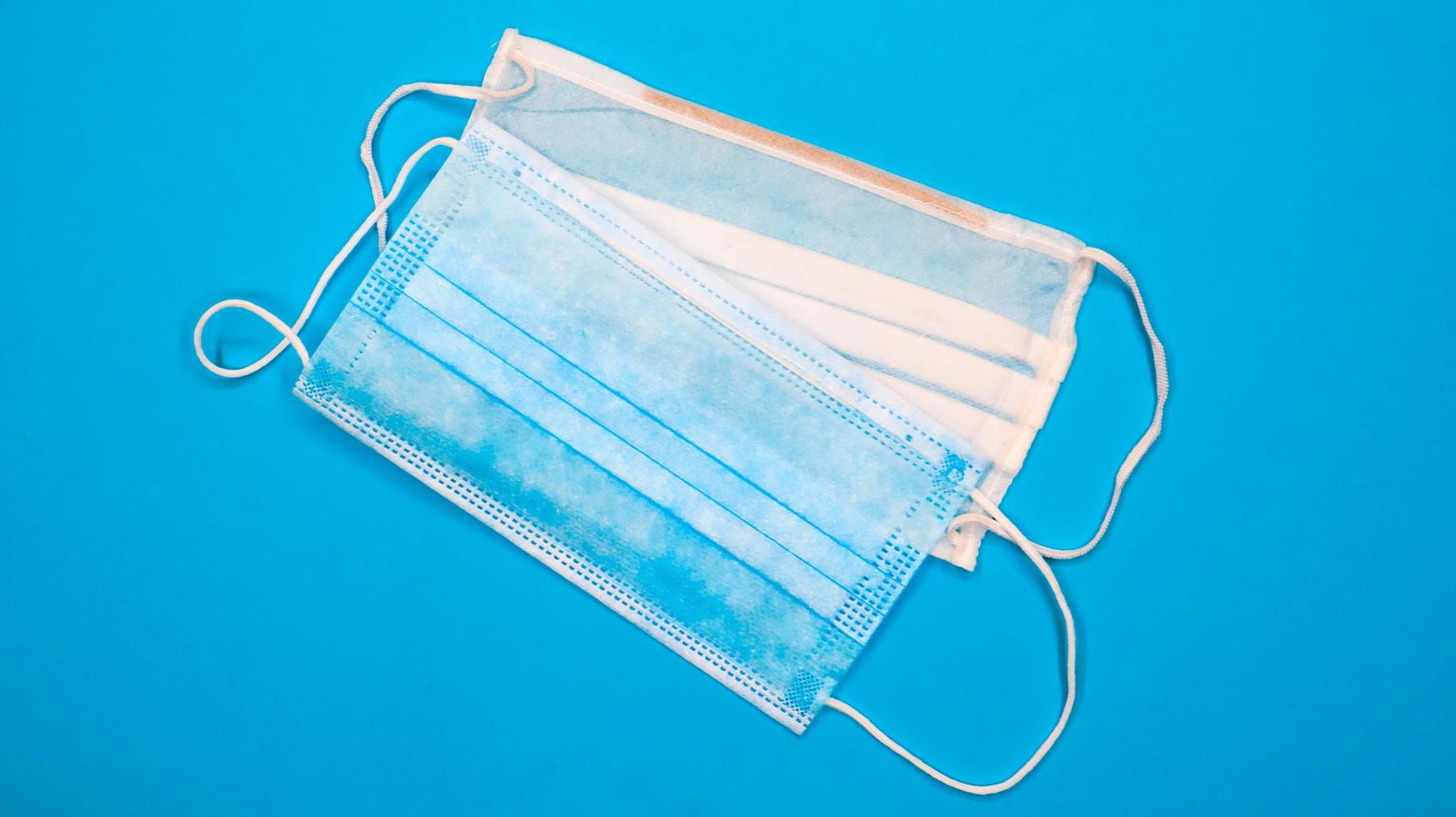 Two three-layer disposable surgical face masks with rubber pads to cover the mouth and nose against a blue background. The concept of protection from bacteria, healthcare and medicine. COVID-19 photo