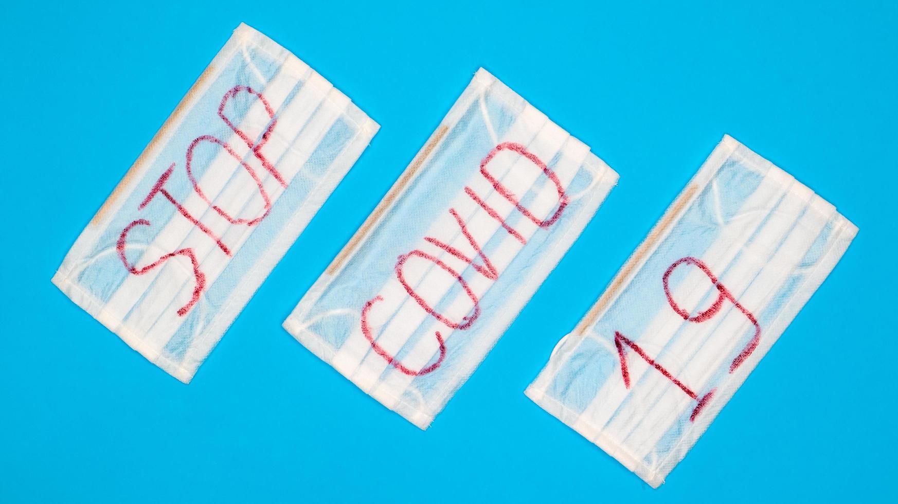Typical 3-ply white surgical mask with rubber earhooks to cover mouth and nose with English block letters Stop Covid-19 on a blue background. Dangerous virus and quarantine concept photo