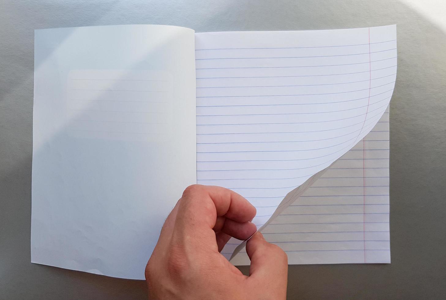 concepto de diseño: vista superior de una mano masculina de alta calidad hojeando una hoja de cuaderno de rayas azules. vista superior, espacio de copia, endecha plana foto