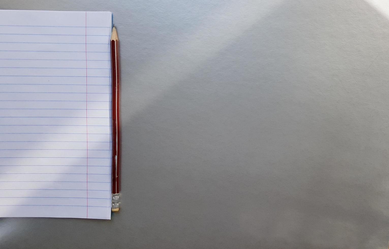 open school notebook with pen on a gray desk with sun rays from the window. A blank, white sheet of notebook for writing. education concept. Copy space. view from above. Flat lay photo