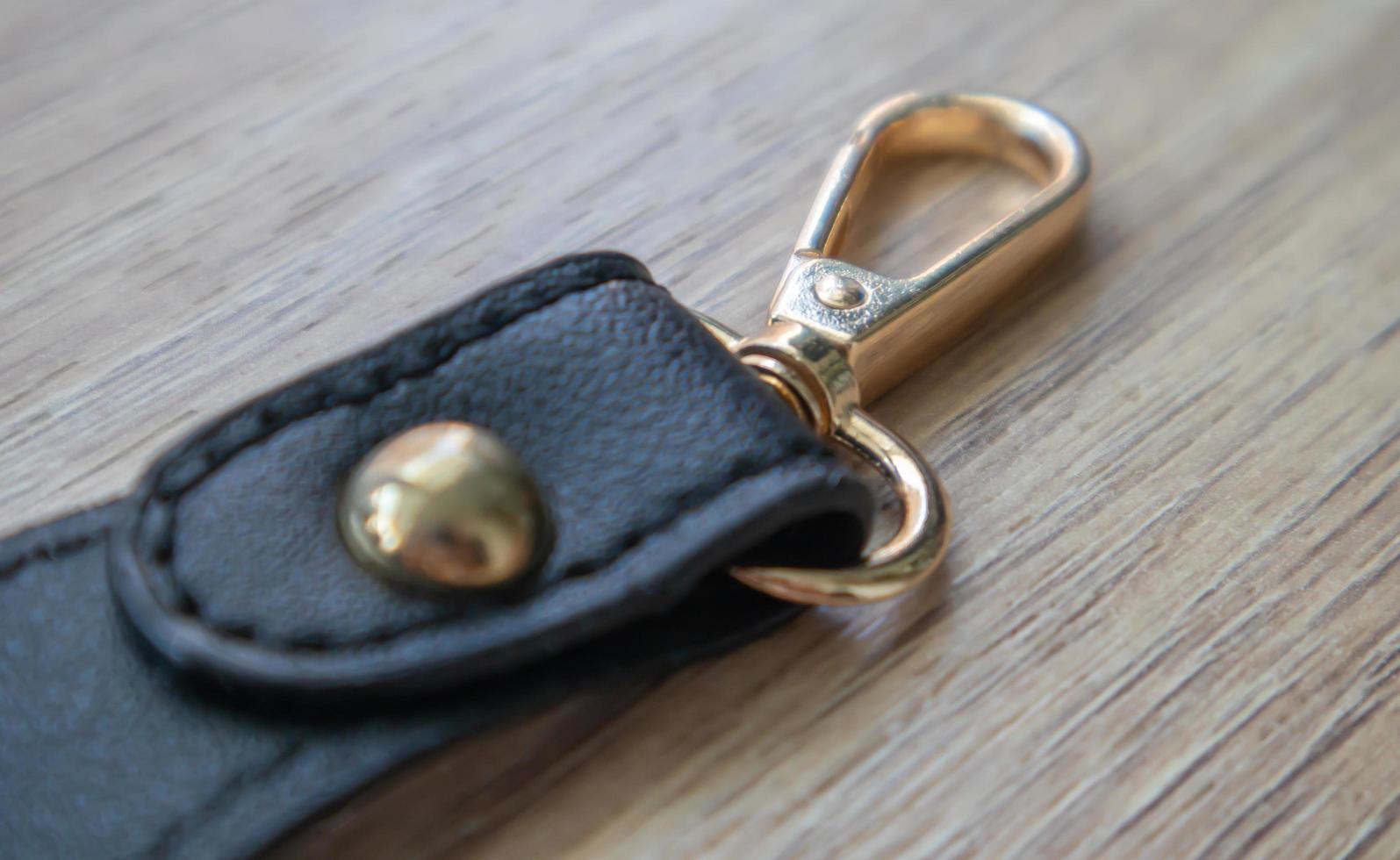 Swivel carabiner fastener with leather black bag strap on a wooden background. Metal carabiner with swivel clip or hook. Small gold fittings close-up in selective focus. photo