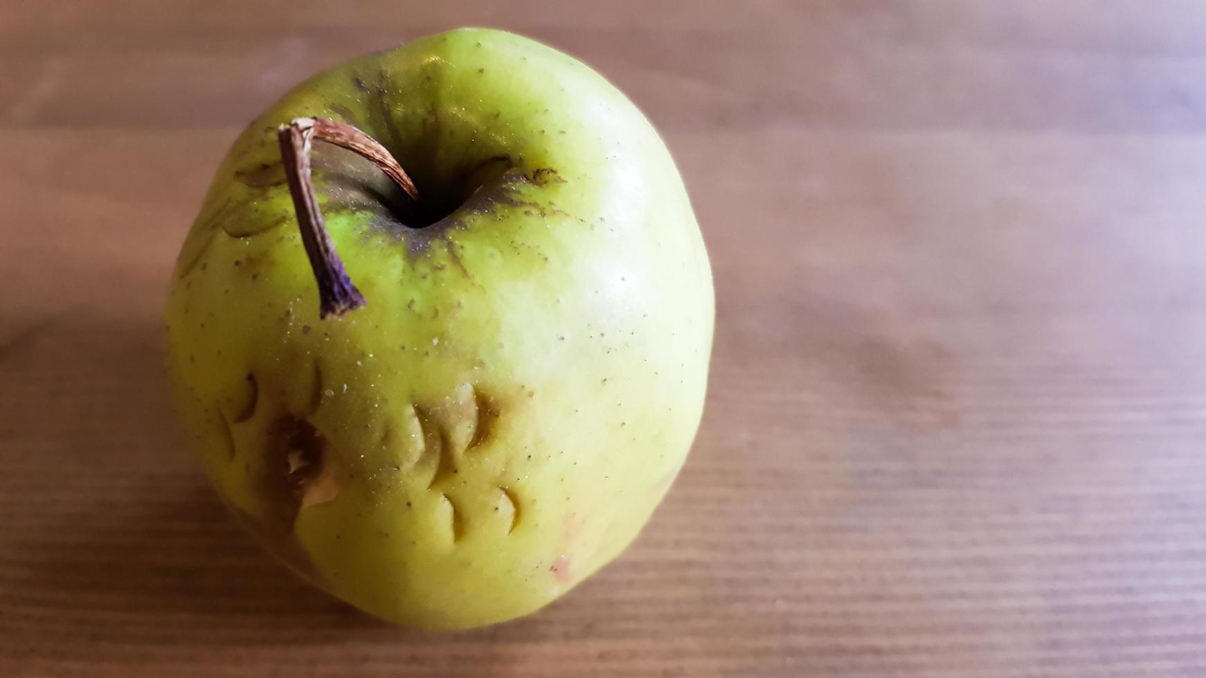 green rotten apple on a wood background. Green apple on a old wooden background, top view. Organic juicy bio apple ugly, with defects edible lies on a wooden table. No ugly food photo