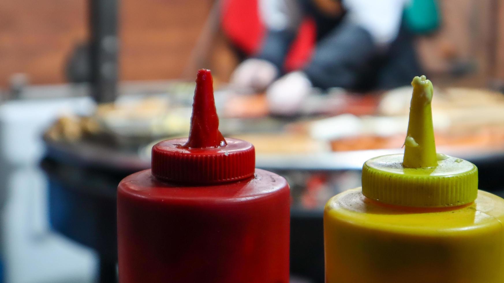 salsa de tomate y mayonesa en tubos de plástico cerca de una parrilla de la calle en primer plano en primer plano con enfoque selectivo. barbacoa, festival de comida callejera. dos latas de salsas de carne. Envase rojo y amarillo. foto