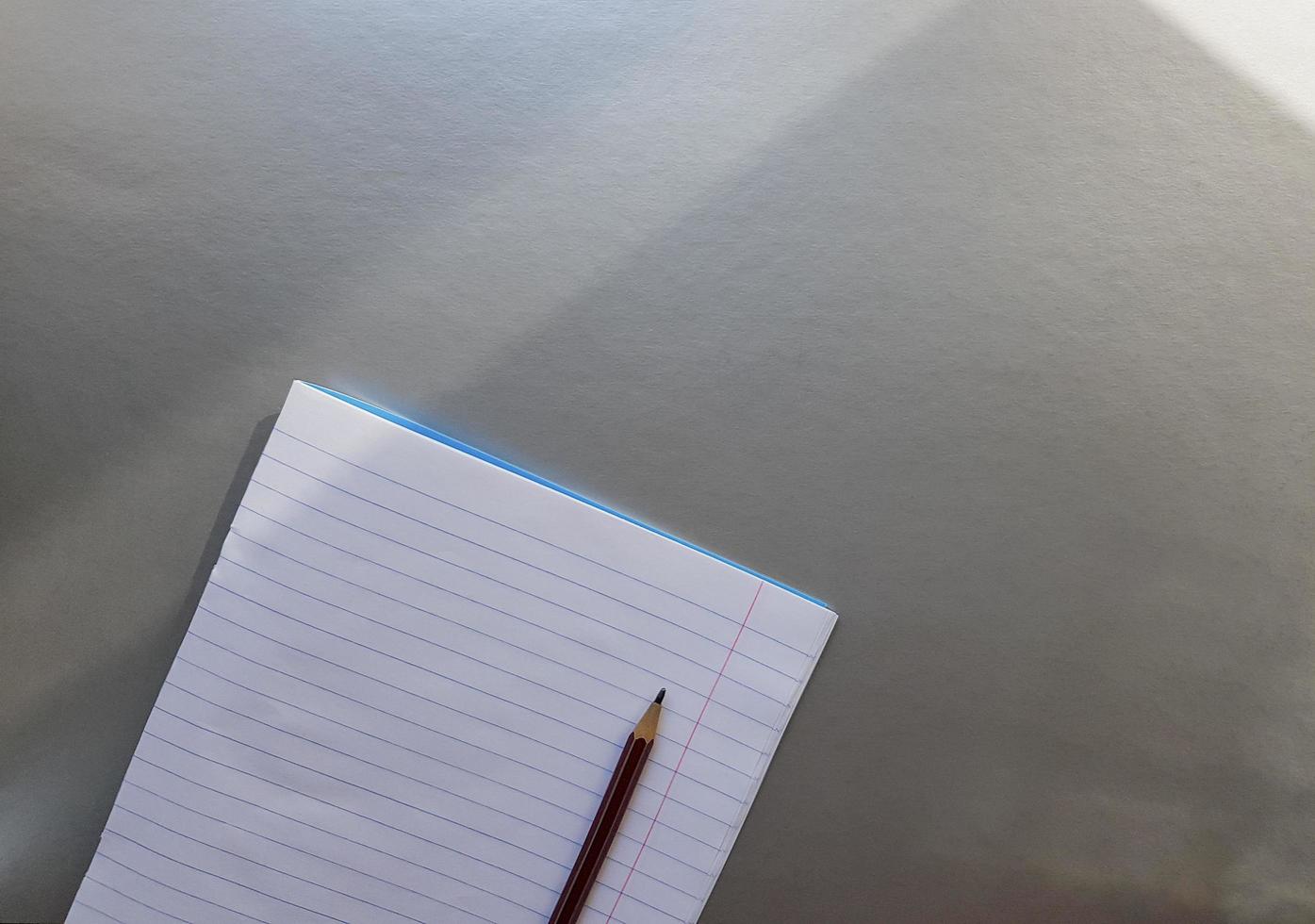 cuaderno escolar abierto con bolígrafo sobre un escritorio gris con rayos de sol desde la ventana. una hoja de cuaderno en blanco para escribir. concepto de educación. copie el espacio. vista desde arriba. endecha plana foto