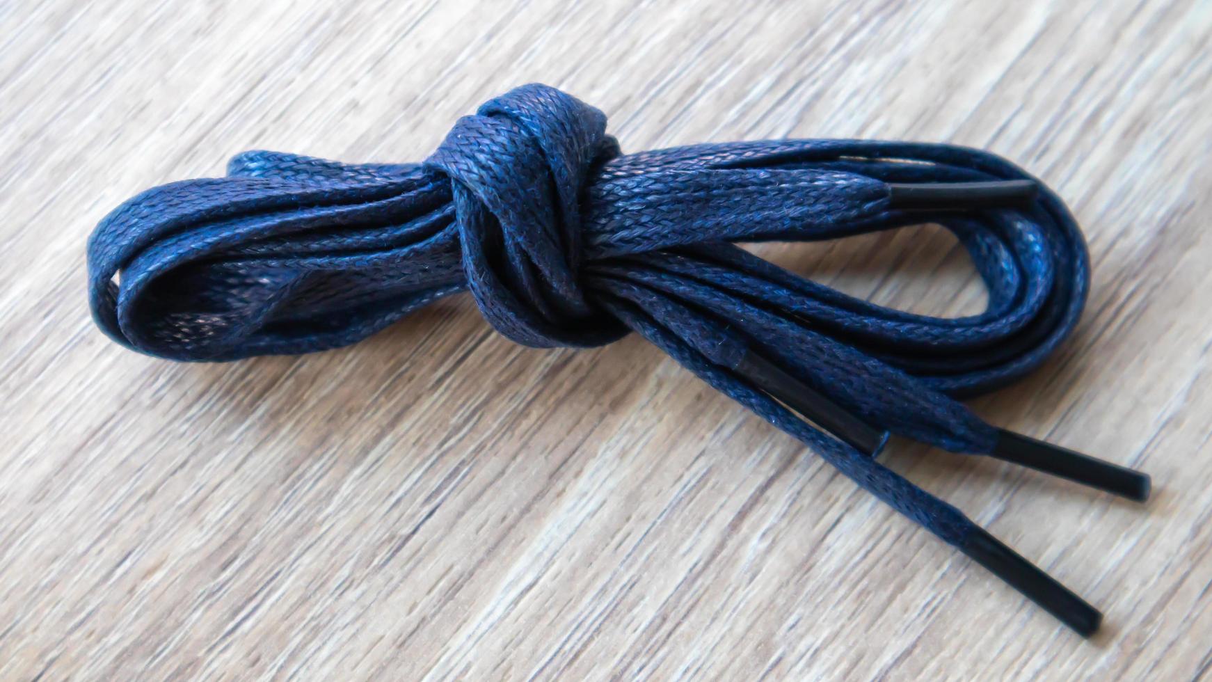 A subject shot of dark blue flat laces with thin tips for shoes rolled up and isolated on a wooden background. Stylish accessory. photo