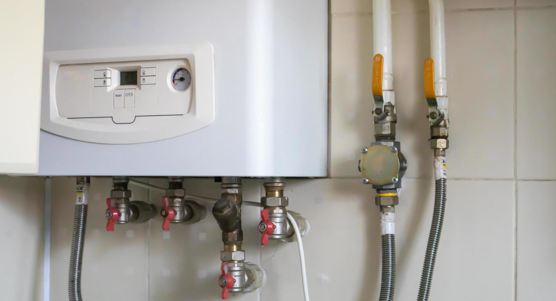 A gas double-circuit boiler is installed in the apartment. Autonomous heating boiler with a control panel, buttons, a display with temperature readings and red valves on pipes in a home kitchen. photo