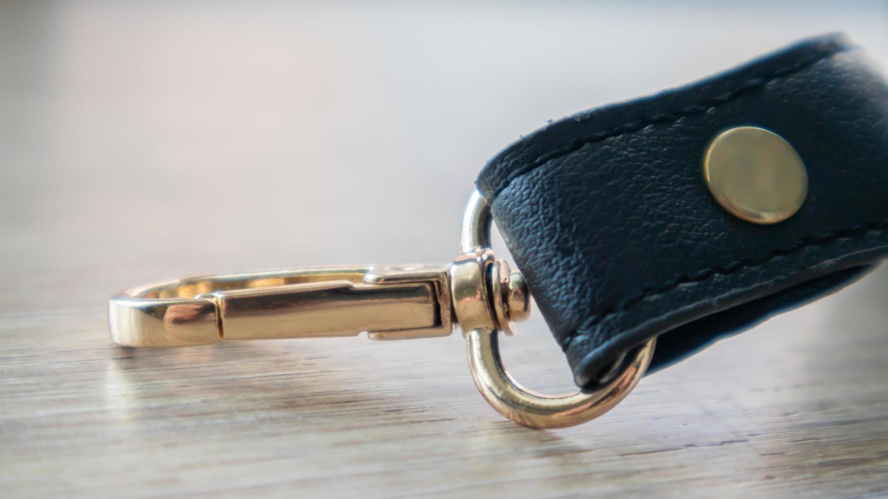 Swivel carabiner fastener with leather black bag strap on a wooden background. Metal carabiner with swivel clip or hook. Small gold fittings close-up in selective focus. photo
