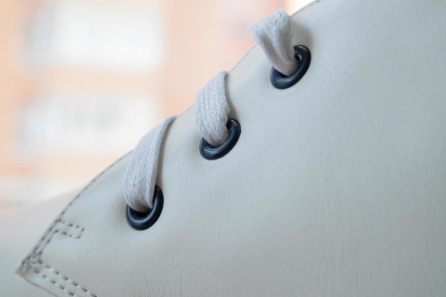 White leather sneakers lace-up shoes. White laces are tied close-up. Blurred background. Sports concept. Metal rivet for shoes as a detail or an element. Fashionable and stylish footwear. photo