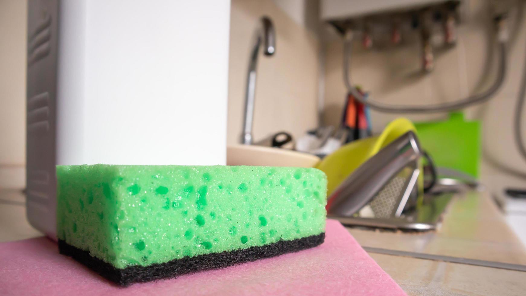 Green sponge and liquid soap dispenser for washing dishes on a dirty sink completely with dishes and kitchen utensils. Washing dishes in the kitchen by hand with detergent and a sponge. photo