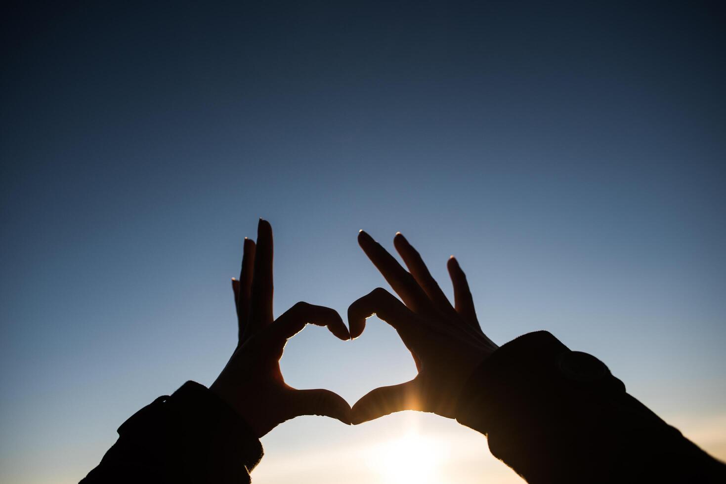 Silhouette hands forming a heart shape with sunrise photo