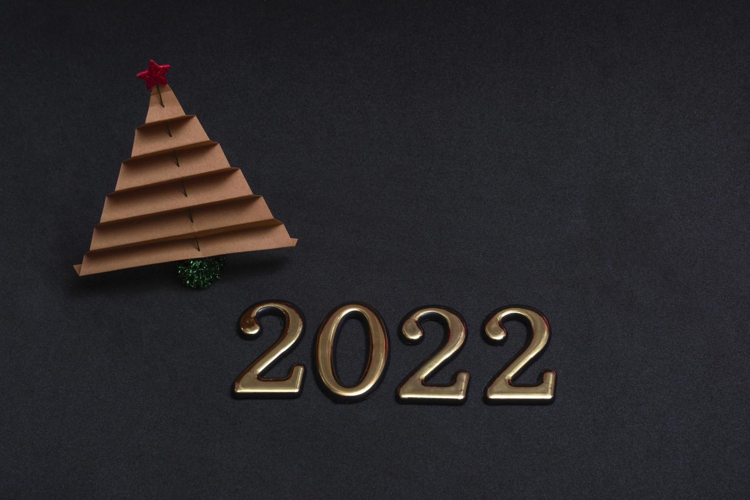 composición de año nuevo. Árbol de Navidad de papel marrón con números dorados 2022 sobre fondo negro con espacio de copia. foto