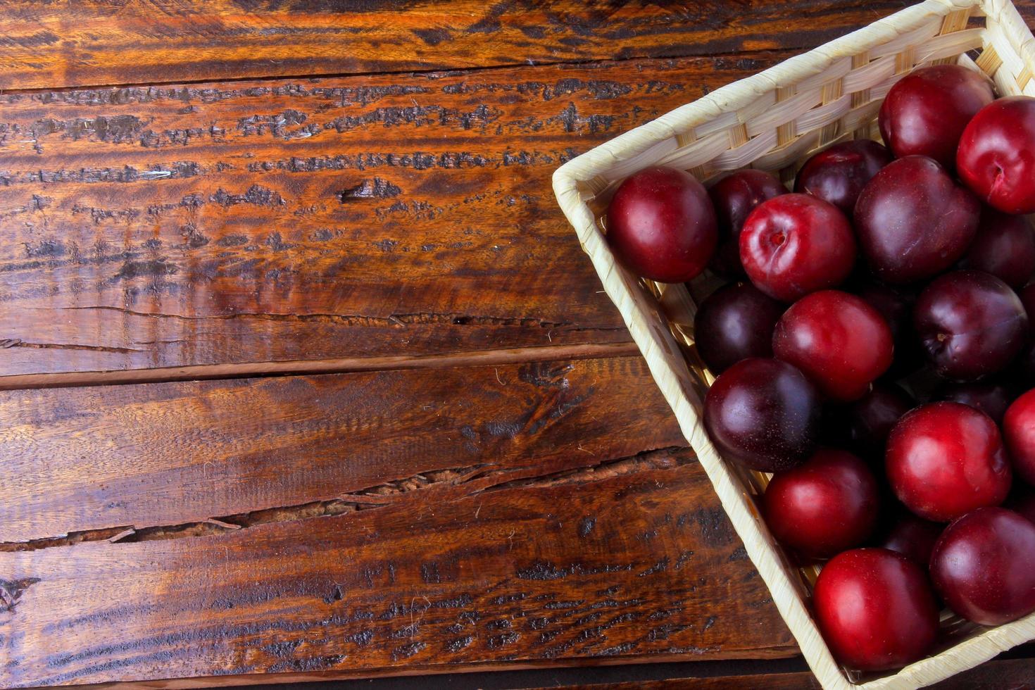 raw and fresh organic plums inside rustic fabric wooden box on rustic table. Copy space photo
