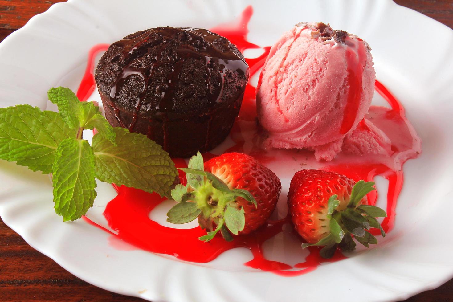 Petit Gateau con helado en un plato blanco con fresa sobre mesa de madera rústica foto