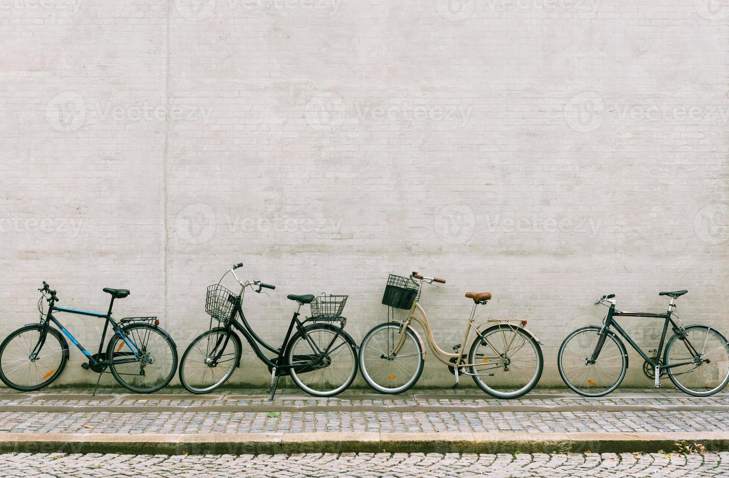 Four bicycles stand near a white brick wall. Several different bikes parked along an empty street in Copenhagen photo