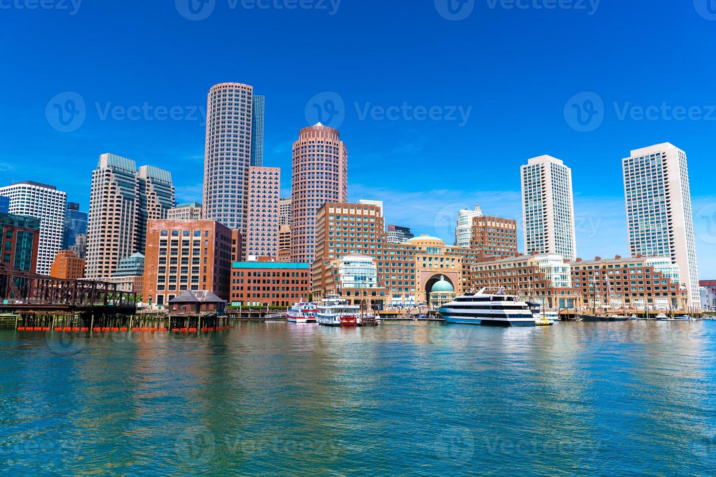 Boston paisaje urbano reflejado en el agua, rascacielos y edificios de oficinas en el centro de la ciudad contra el cielo azul claro, vista desde el puerto de Boston, EE. foto