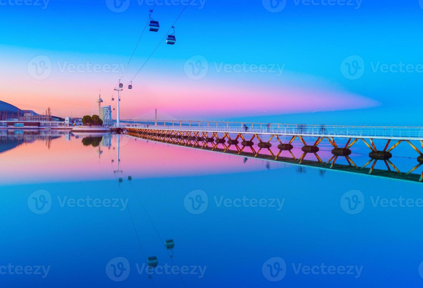 Picturesque sunset over The Park of the Nations in Lisbon, Portugal. Evening cityscape with cable car road and bridge reflected in water photo