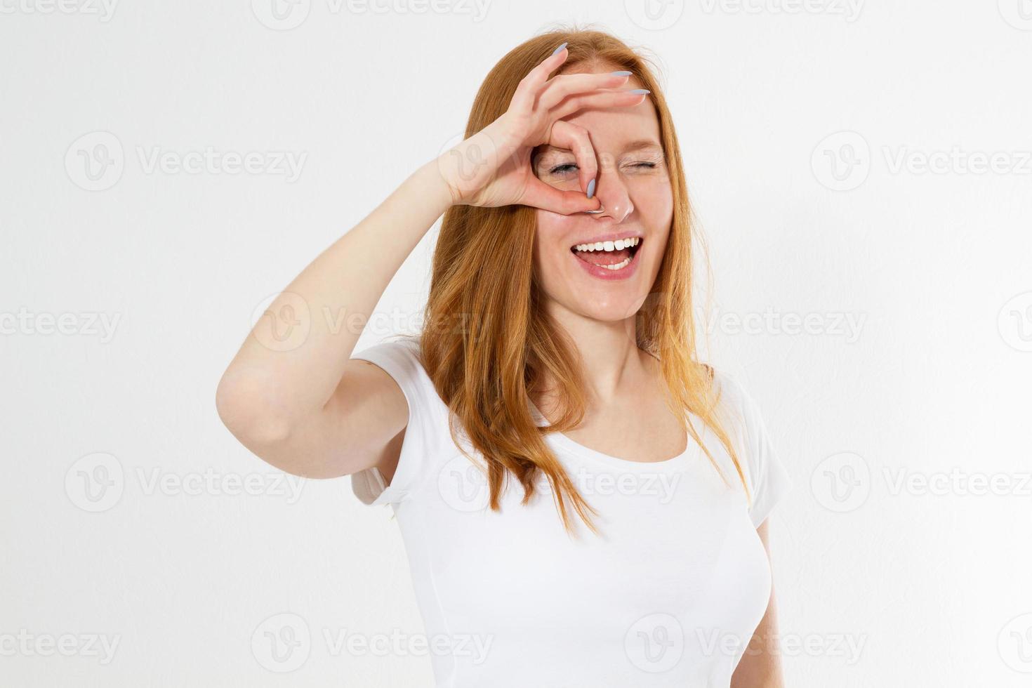 Red head girl in colorful clothing holding her fingers around the eye copy space isolated, young woman shows okays and looking through photo